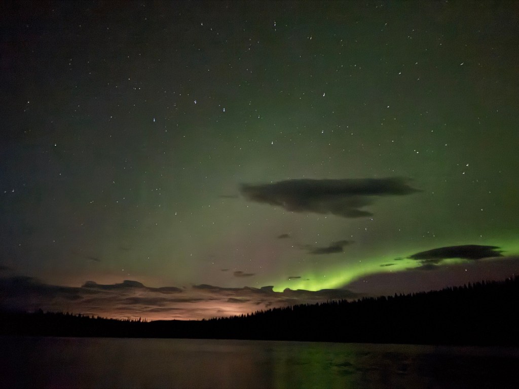 green and orange colored northern lights over a lake