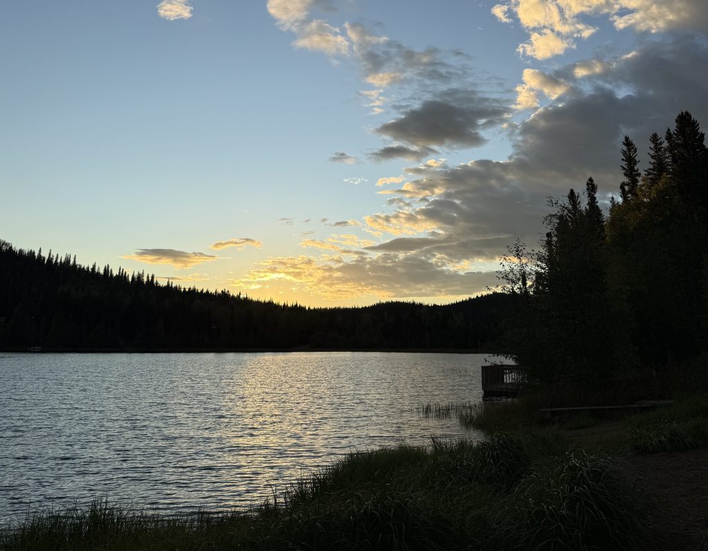 a lake with a sunrise behind the trees